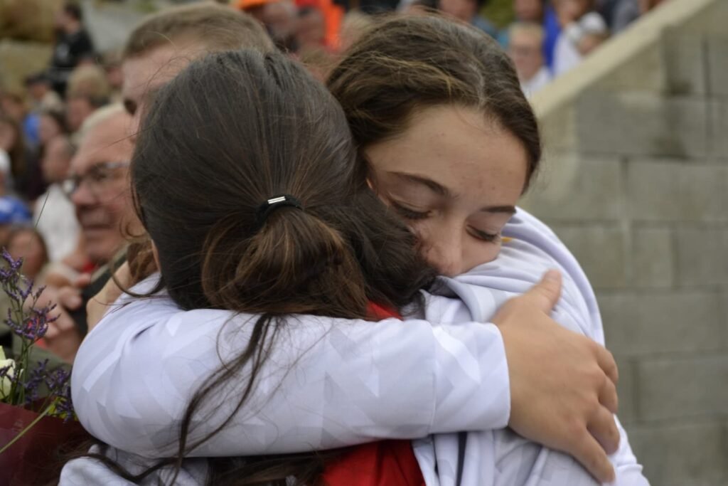 Two young kayak polo players embracing tightly after a match, faces hidden in the hug.