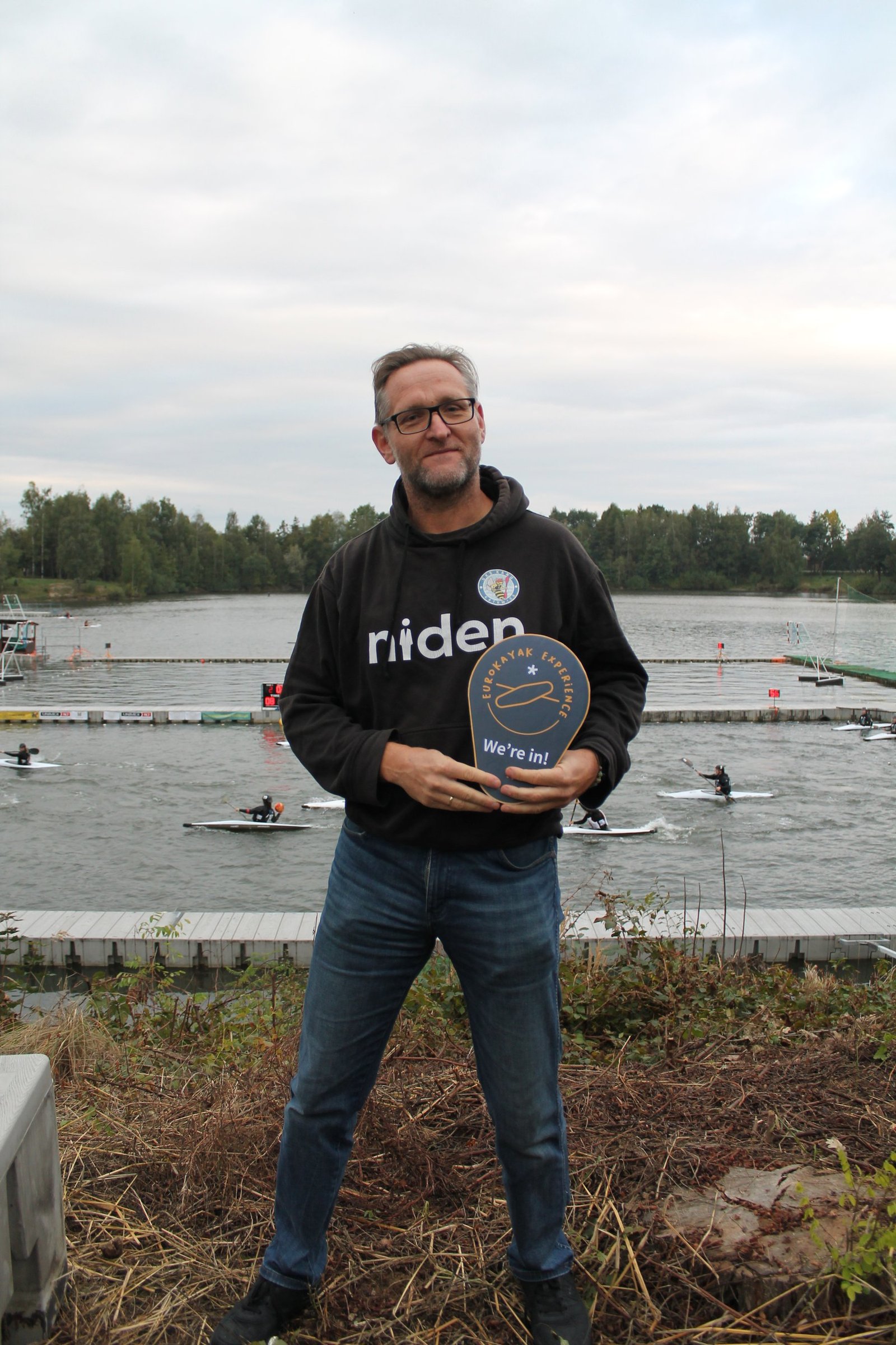 The representative of the Katowice club standing by the tournament pool in Poland, holding a 'EuroKayak Experience — We're in!' sign.