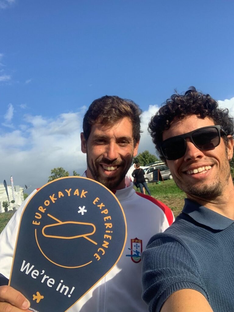 Telmo and a coach from Portimao, now playing for Club Kayak Polo da Barra, smiling and holding a 'EuroKayak Experience - We're in!' sign outdoors.